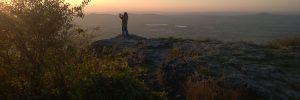 Weiter Blick in die Ferne von einem Berg aus, auf dem ein Mann steht und den Sonnenuntergang fotografiert
