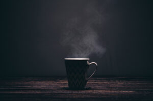 Dampfende Tasse Kaffee im Gegenlich vor dunklem Hintergrund